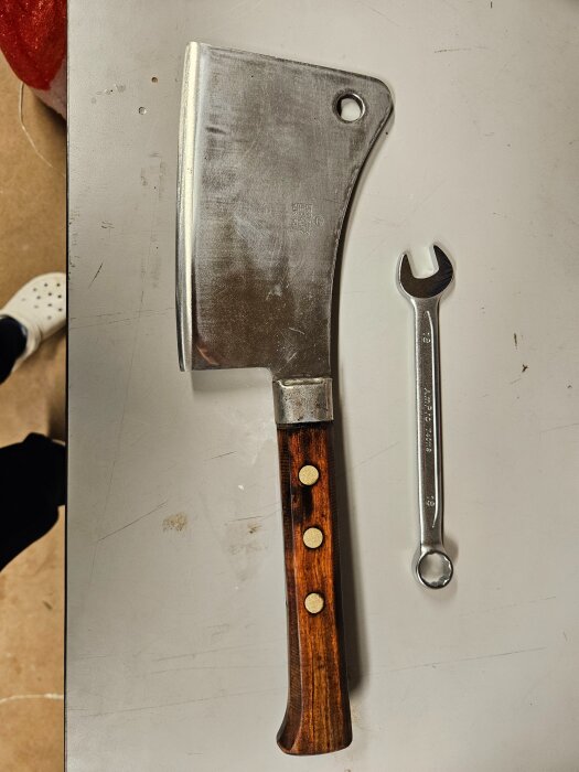 Slipad och oljad köttyxa med trähandtag bredvid en 18-nyckel på vit bakgrund för storleksjämförelse.
