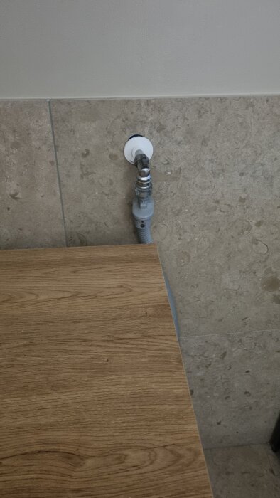 Väggmonterad avloppsslang och rördel ovanför ett träbord i badrummet.
