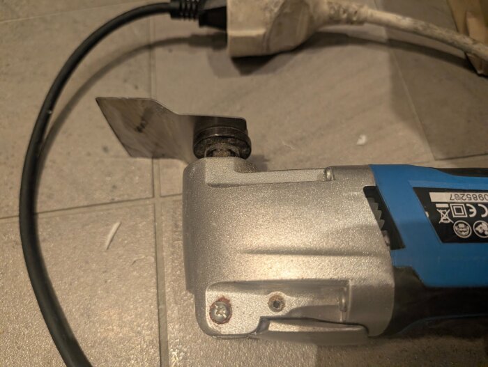Multiverktyg med knivblad på grått kakelgolv, användes för att ta bort siliconfog vid handfatsrenovering.