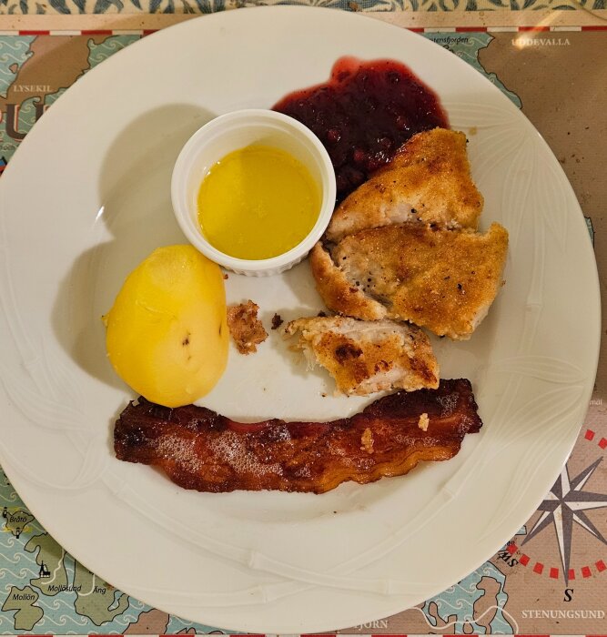 Dubbelpanerad torskfilé med kokt potatis, bacon, smält smör i skål och lingonsylt på vit tallrik.