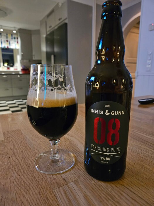 En flaska Innis & Gunn Vanishing Point 08 med ett glas mörk öl på ett träbord i ett kök.