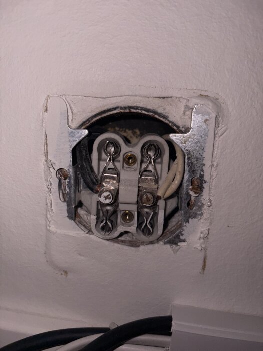 Gammalt dubbelt vägguttag installerat i vit vägg, visande interna kopplingar med kablar anslutna under skruvar.