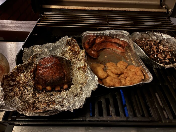Revbensspjäll i folie, korv och kroketter på en grill, redo för servering efter att ha kryddats och glazats med Hickory och BBQ-sås.