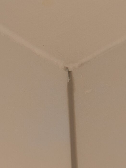 Närbild av ett hörn med ojämna och flisade plattskarvar, ojämn fogning och defekta plattor, vilket indikerar slarvigt utfört arbete i ett badrum.