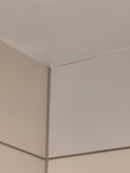 Närbild av ett hörn i ett badrum med kakel, där fogarna är ojämna och kanterna på plattorna ser felkapade och flisade ut.