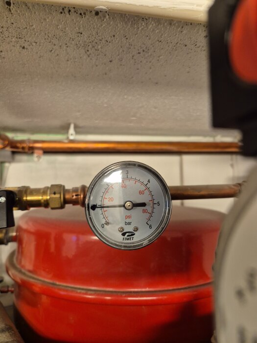 Tryckmätare med visar på 1 bar och 15 psi, synlig på en röd tank i ett hus för anslutning till bergvärmepump.