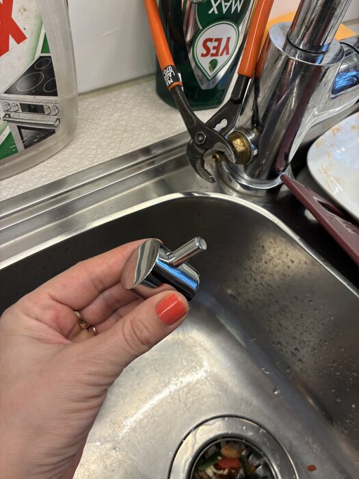 Person håller ett metallhölje bredvid kran med fastklämd tång i kök. Problematik med att skruva fast höljet på kranen.