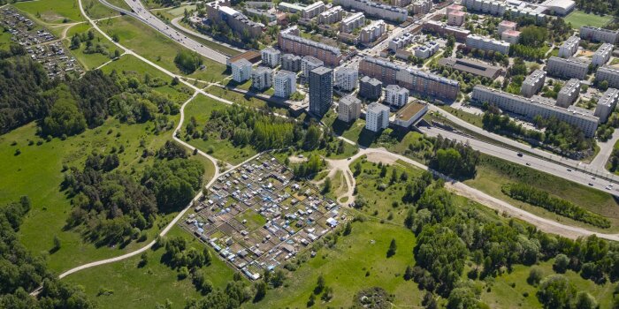 Flygbild över ett område med flerbostadshus, en koloniträdgård och omgivande grönområden.