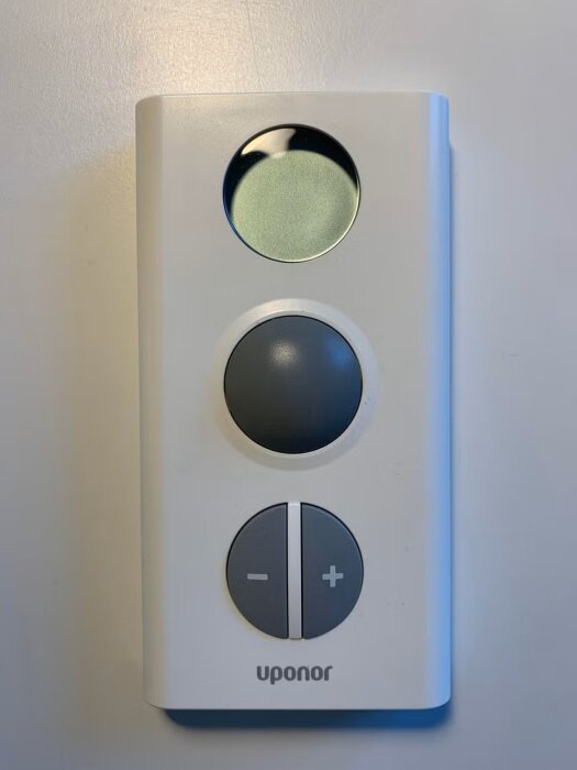 Uponor termostat med tre knappar, inklusive en svart och en grå, samt plus- och minusknappar, mot en vit bakgrund.