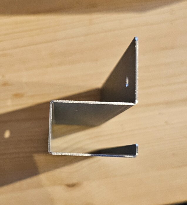 Metallbeslag i Z-form med förborrat hål, används för att fästa fläkt i köksskåp enligt instruktioner.