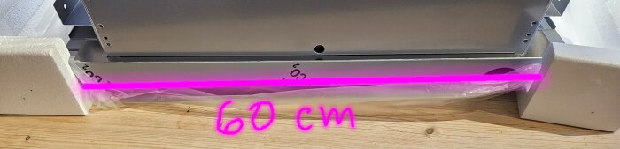 Fläktdel med rosa markering och text "60 cm" liggande på träskiva, omgiven av frigolitstöd på sidorna.