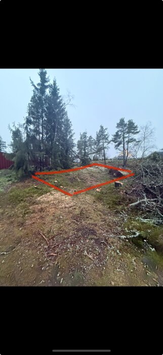 Markområde avgränsat med röd linje, omgiven av träd, med potentiellt berg i dagen för garagebygge.