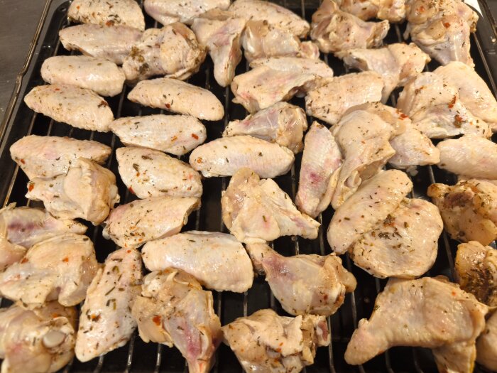 Rå kycklingvingar ligger på ett ugnsgaller, marinerade i en brine med kryddor som chili, timjan och rosmarin, redo för tillagning i ugn.