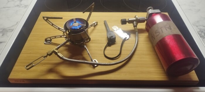 Primus Multifuel kök på en skärbräda med gasbehållare och tändverktyg, redo för friluftsliv och matlagning.