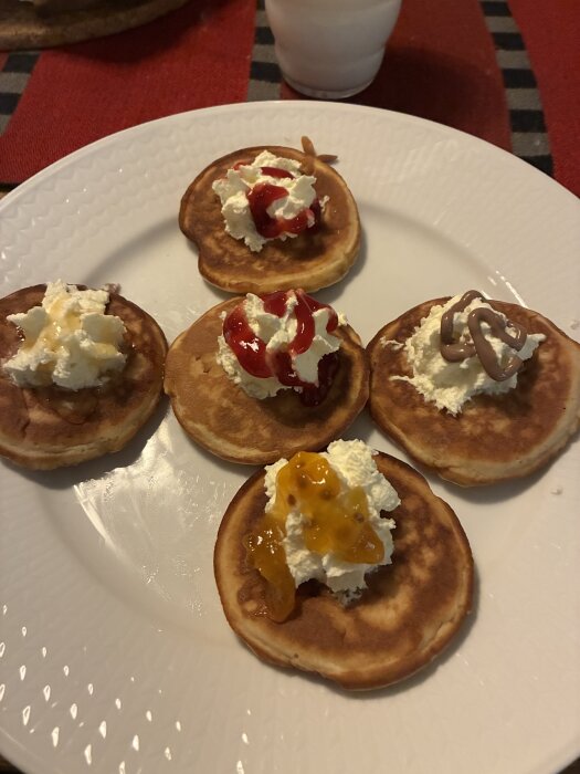 Små pannkakor med vispad grädde och olika toppingar, inklusive honung och mörk sirap, på en vit tallrik.