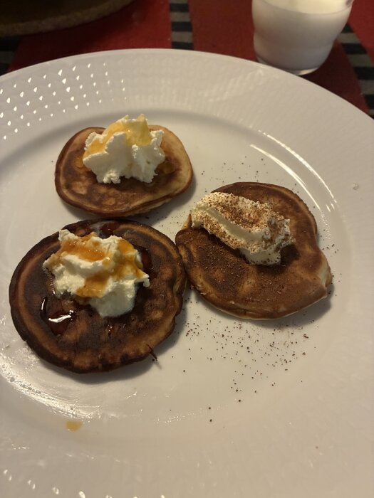 Små pannkakor med grädde, honung och sirap på en vit tallrik. Glas mjölk i bakgrunden.