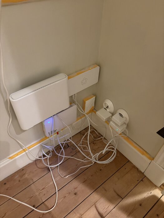 Hörna med teknisk utrustning och kablar på trägolv, omgiven av vägguttag.