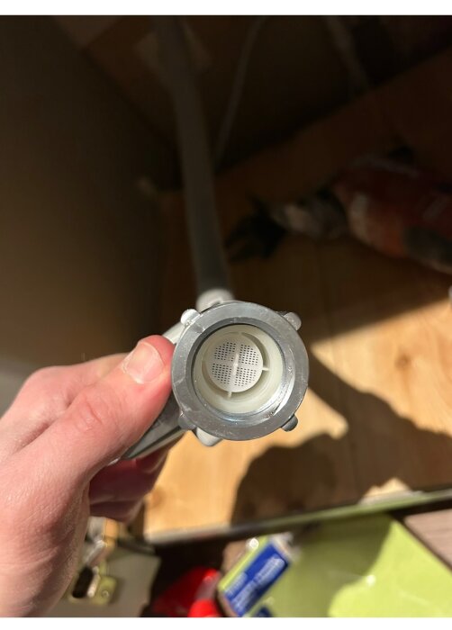En hand håller en slang med en ventil i fokus, troligen för anslutning av en diskmaskin under installation.