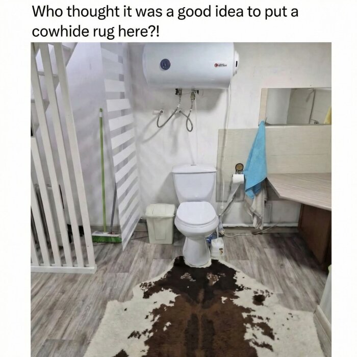 WC med en ko-skin matta framför toalett, vit vägg, blå handduk på handfat.