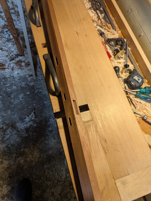 Närbild av en träbänk med verktyg och träbitar. Synliga fogar som tapp och tapphål visar ett pågående byggprojekt.