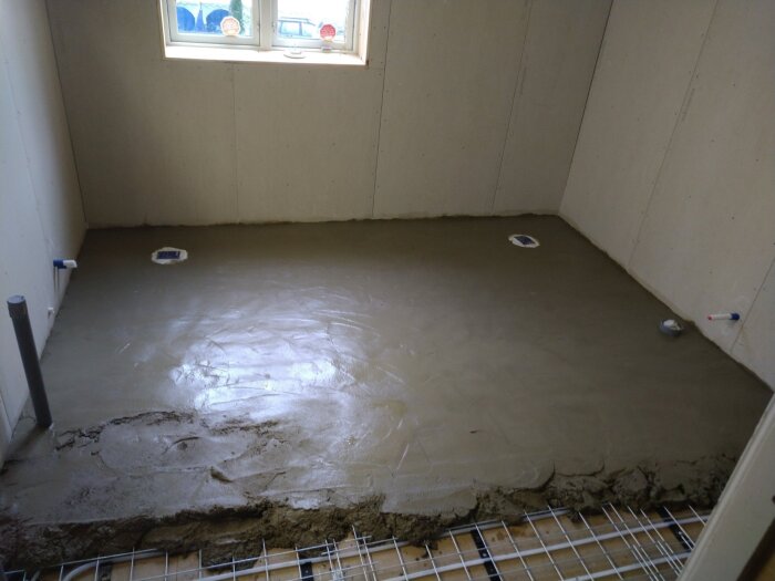 Nygjuten betonggolv i ett rum med vita väggar och ett fönster i bakgrunden.