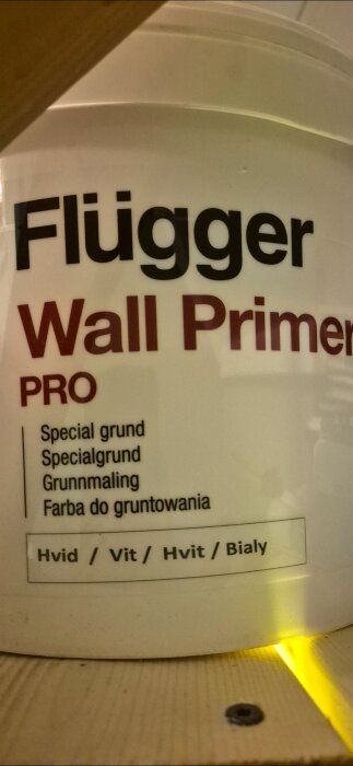 Burk med Flügger Wall Primer pro, en specialgrundfärg i vit nyans, stående på ett bord.