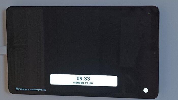 En tablet på väggen visar tid och datum, 09:33 måndag 19 jan. Skärmen är delvis svart med en text om att en IP-webbkamera övervakar området.