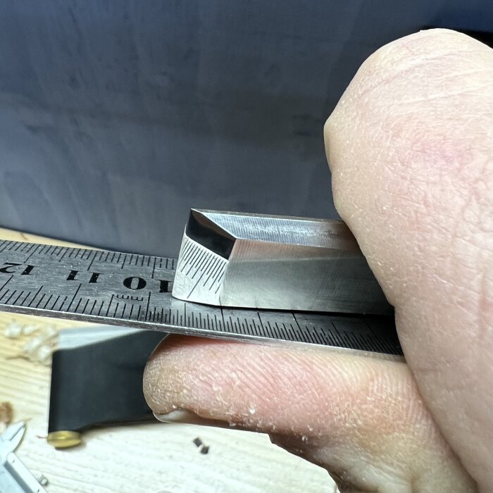 Bilden visar en hand som håller ett stämjärn mot en linjal, med fokus på den slipade eggen.