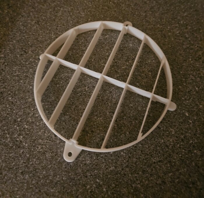 Vit plastgallerbit ligger på en stenliknande yta, del av ventilationssystem.