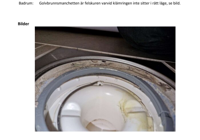 Golvbrunn med felaktigt monterad manschett där klämringen inte sitter korrekt, vilket potentiellt kan orsaka läckage eller andra problem i badrummet.