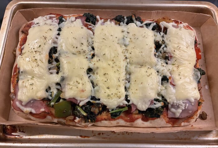 Hemlagad pizza med smält ost på toppen, fylld med paprikor, svartkål, gul lök, purjolök och pumpakärnor på ett bakplåtspapper.