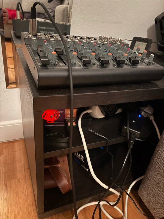 Rullbar hurts med mixerbord och kablar, delvis utrullad mellan soffa och vägg, med ett grenuttag och musikutrustning på hyllorna.