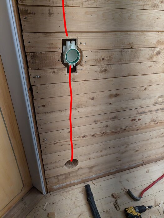 Vägg av liggande råspont med hål för eldosor och markerad linje för VP-rörinstallation, verktyg och sågspån synliga på golvet.