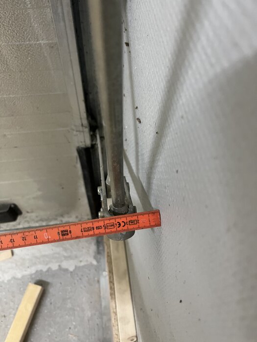 Mätning av avstånd mellan garageportens stag och väggen med hjälp av ett måttband.