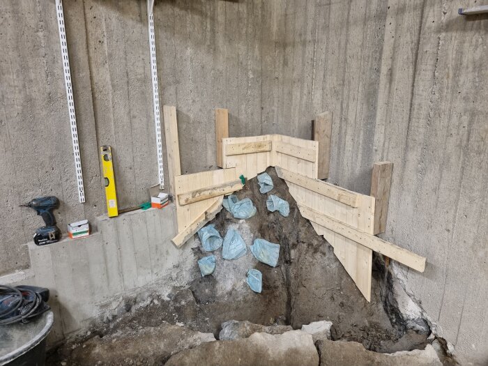 Träkonstruktion för formning av betongvägg i ett pågående byggprojekt. Verktyg och material syns bredvid, inklusive en borr och ett vattenpass.