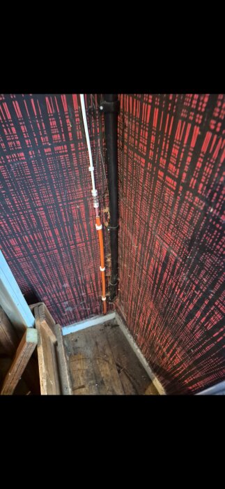 Fiberkabel installerad längs väggen i ett rum med röd- och svartrandig tapet, visar anslutning ovanför ett trägolv.