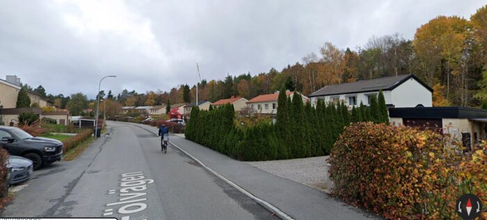 Gata i Järfälla med 1960-talsbebyggelse, spritputsade småhus i olika färger och en cyklist på vägen, omgiven av höstfärgade träd.