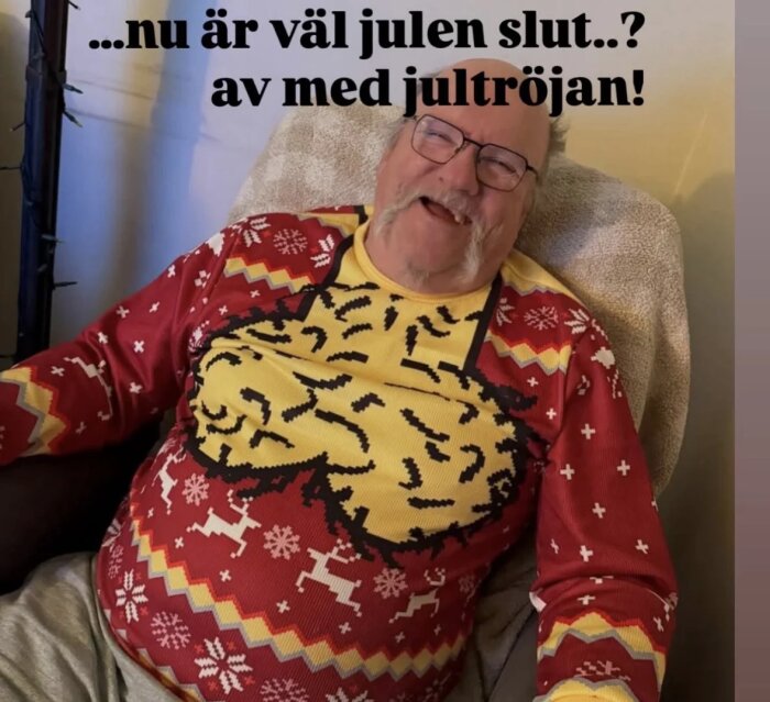 Man i röd jultröja med ett skrattande motiv, sitter i en stol, text ovan: "...nu är väl julen slut..? av med jultröjan!