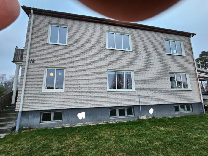 Flerfamiljshus i tegel med källarfönster och vita märken på fasaden som markerar var nya ventilationshål planeras.