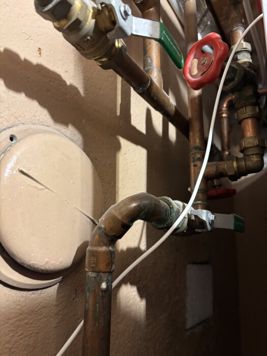Rörsystem med kulventiler och rattar i ett utrymme, kopplade till golvvärme och radiatorer, med fokus på volymmätning av ett kärl.