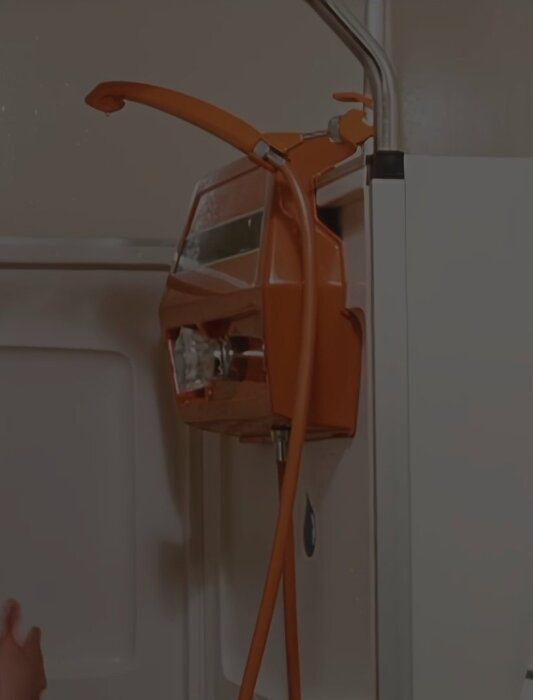 En orange duschinstallation med slang och munstycke från en reklamfilm, typ 1972, i ett modernt badrumsmiljö i Stockholm.