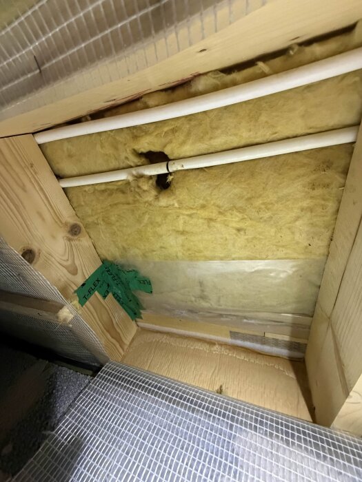 Underlagsbild med två rör genom isolering, hål i isolering och grön tejp vid rörgenomföring.