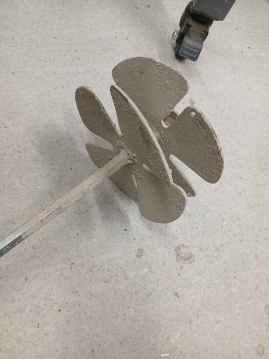 En cementblandare med flera paddlar ligger på ett betonggolv, del av ett verktyg för mixning av material i byggprojekt.