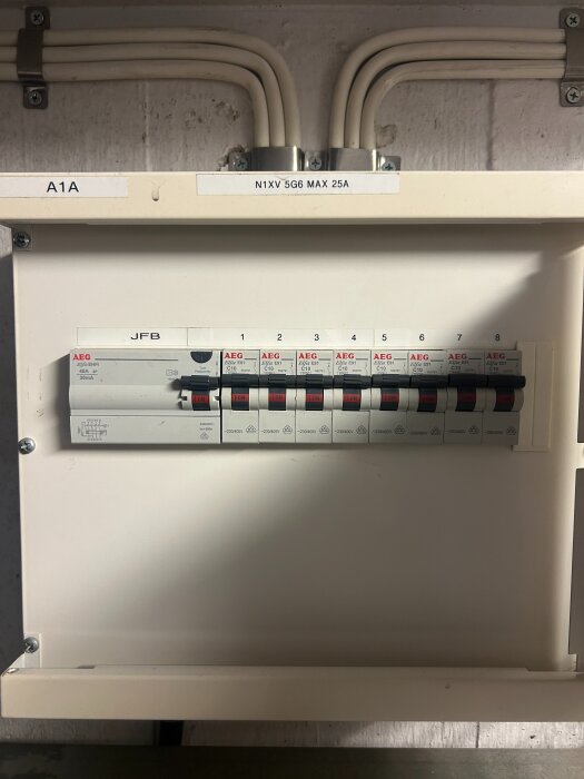 Elcentral i f.d. tvättstuga med flera vita kablar och åtta brytare. Panel märkt med "N1XV 5G6 MAX 25A" och brytare från AEG.