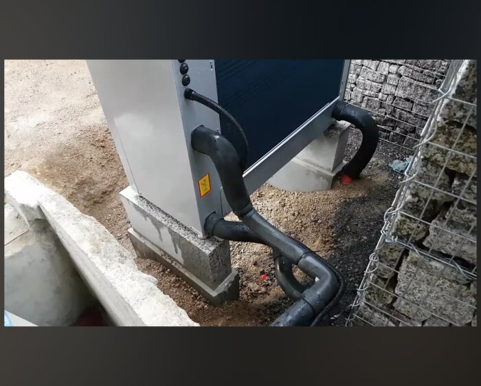 Utomhusinstallation av VVM310 och F2120-16 med synligt kondensvattenrör utan isolering vid grus och stenar.