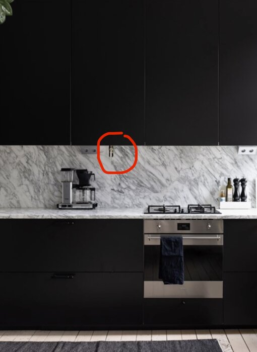 Kök med svart skåpinredning, marmorskiva och mosaikvägg. Röd cirkel markerar en gasventil ovan bänkskivan.