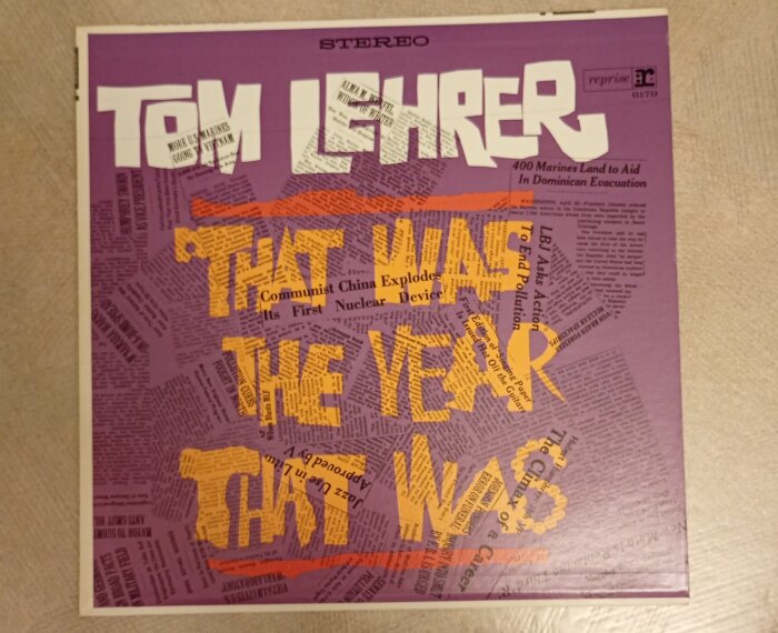 Vinylskivomslag med texten "Tom Lehrer" och "That Was The Year That Was" i stora bokstäver, omgiven av tidningsartiklar på lila bakgrund.