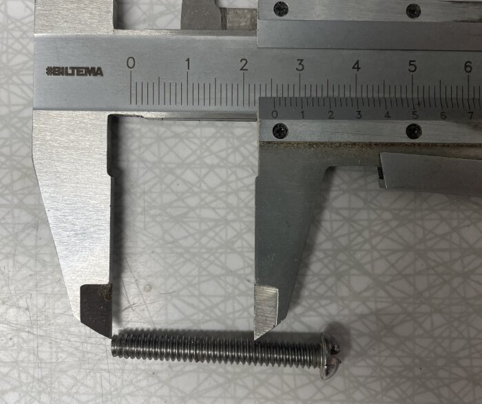 Skjutmått mäter en skruv med 4,67 mm diameter på ett mönstrat bord.