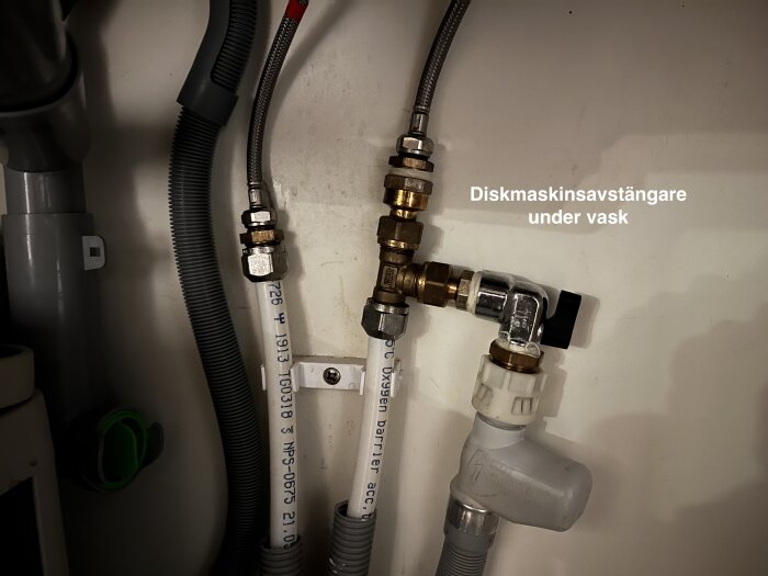 Diskmaskinsavstängare under en vask, med anslutna rör och kopplingar synliga.