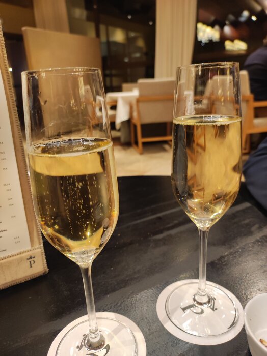 Två glas bubbel på ett svart bord i en restaurangmiljö.